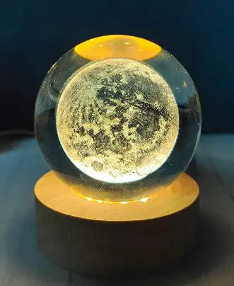 A USB crystal ball night light glowing with a warm light, resembling a birthday cake with candles on top, placed on a wooden surface.