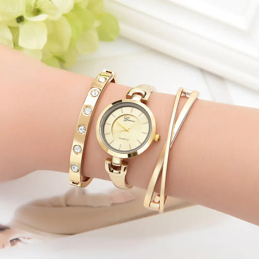 A woman's wrist wearing a gold-colored bracelet and quartz watch with a white dial, surrounded by two additional gold bracelets with crystal embellishments.