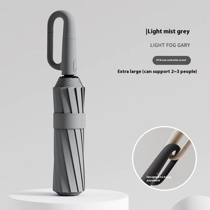 A white umbrella with a ring buckle, standing on a white surface, with a close-up inset showing the texture of the umbrella's fabric.