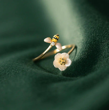 A 925 silver ring with a bee design on top, placed on a green fabric background.