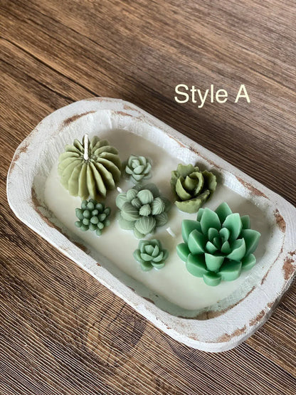 A wooden bowl containing a scented cactus garden candle with various artificial cactus shapes in green tones.