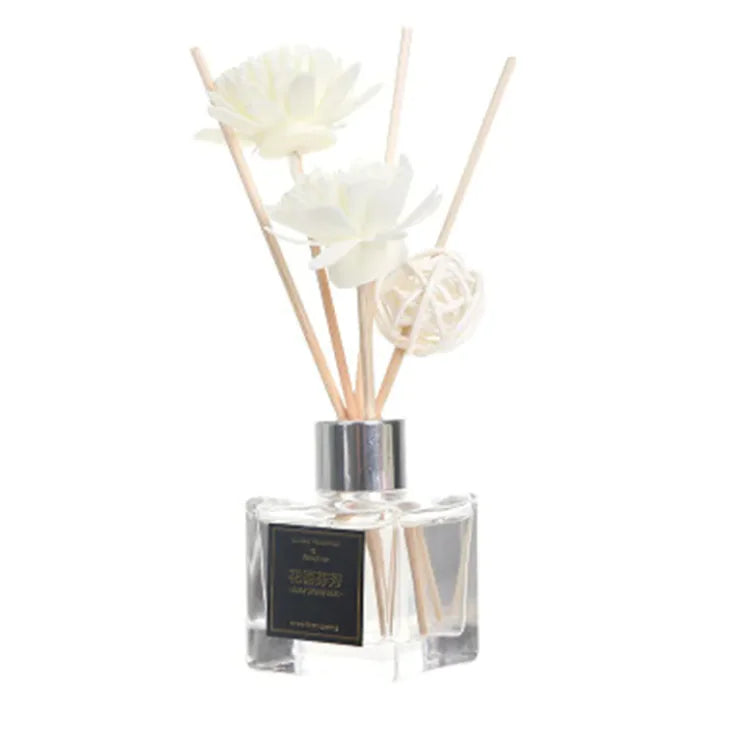 A glass aromatherapy bottle with a white label, filled with water-based essential oils and adorned with white floral rattan sticks.