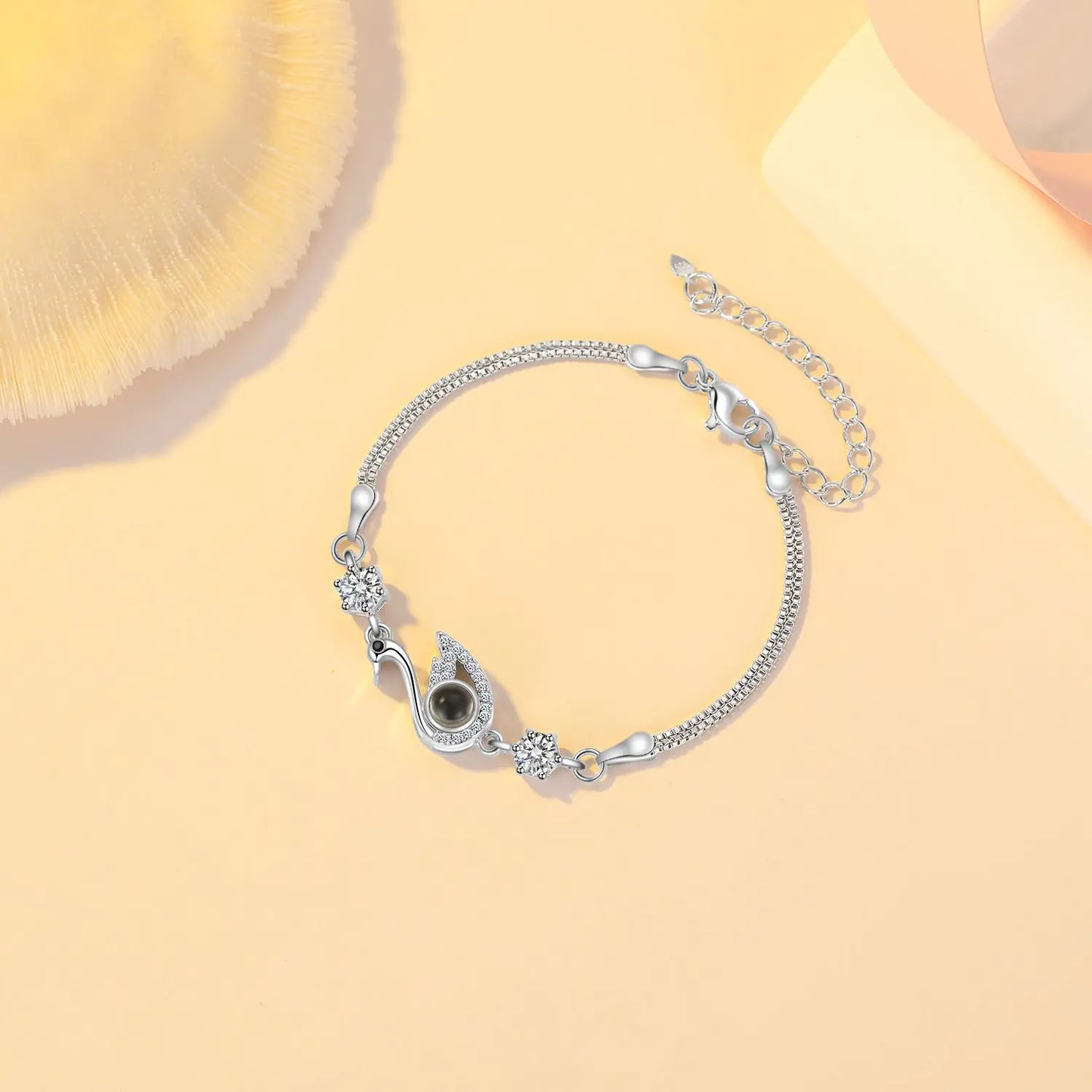 A rose gold-colored bracelet featuring a black swan charm with zirconia accents on a chain-link design, displayed against a beige background.