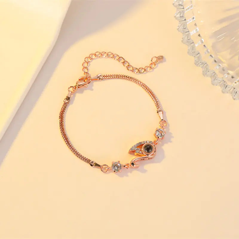 A rose gold-colored bracelet featuring a black swan charm with zirconia accents on a chain-link design, displayed against a beige background.