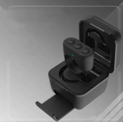 A Bluetooth fingertip remote placed inside its charging case, which is open and showing the remote's battery level indicator.