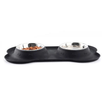 A black silicone pet bowl mat in a bone shape, with two stainless steel bowls placed on it.