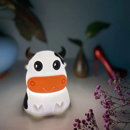 A cartoon-inspired cow-shaped silicone Bluetooth speaker and lamp with LED lighting, displayed in a room setting.