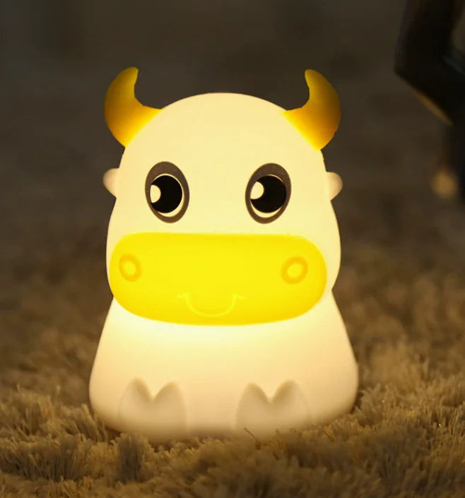 A cartoon-inspired cow-shaped silicone Bluetooth speaker and lamp with LED lighting, displayed in a room setting.