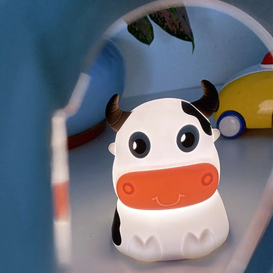A cartoon-inspired cow-shaped silicone Bluetooth speaker and lamp with LED lighting, displayed in a room setting.