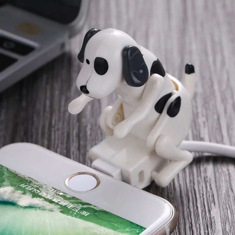 A plastic cartoon dog cable protector designed to cover and protect a charging cable, displayed on a wooden surface next to a smartphone.