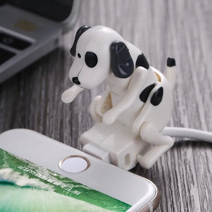 A plastic cartoon dog cable protector designed to cover and protect a charging cable, displayed on a wooden surface next to a smartphone.