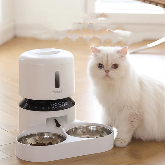 An automatic capsule cat feeder with dual bowls, one for food and one for water, in a white color, featuring a digital display and a cat looking towards the viewer in the background.
