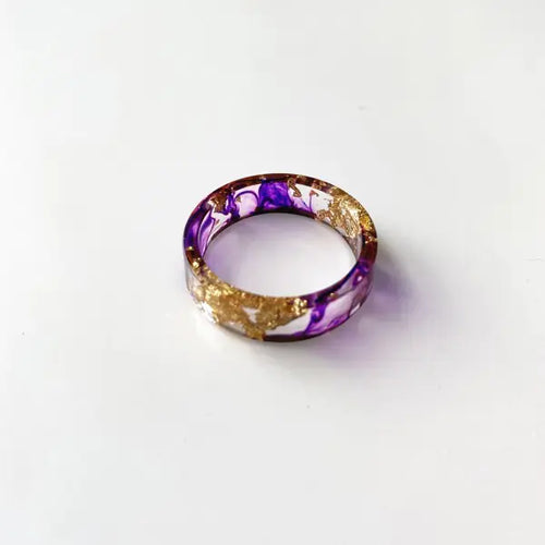 A colorful handmade resin ring with dried flowers and gold foil, displayed on a white background.