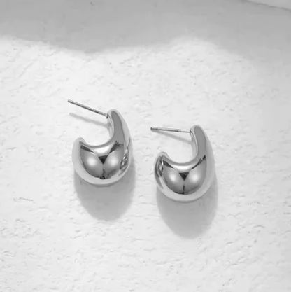 A pair of silver-colored comma-shaped teardrop earrings placed on a white surface.