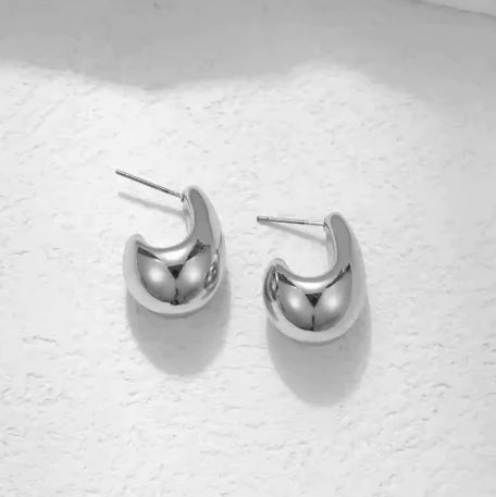 A pair of silver-colored comma-shaped teardrop earrings placed on a white surface.