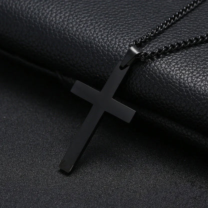 A black cross necklace made of stainless steel, displayed against a black leather background.