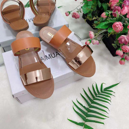 A pair of flat slippers with crossed straps, one featuring a snake skin pattern, the other in a solid color, displayed on a white surface with a box and decorative flowers in the background.