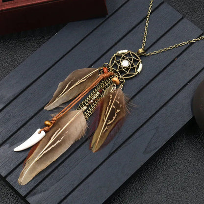 A bohemian feather dream catcher necklace with a round dream catcher design, featuring flowing feathers in brown and white tones, and a white bead at the center.