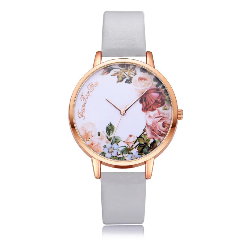 A floral pattern watch with a blue strap and gold-colored case, featuring a white dial adorned with a multicolored floral design.