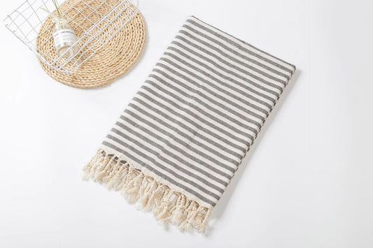 A striped beach towel with fringes displayed flat on a white surface, alongside a woven basket.