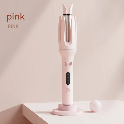 A pink full-automatic hair curler standing upright on a stand with a closed curling chamber, displaying its body and temperature control panel.