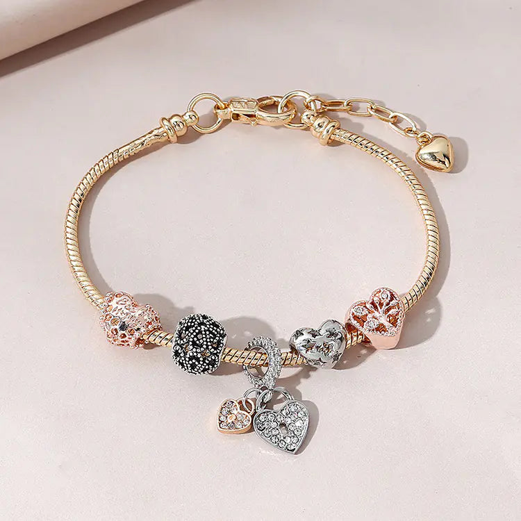 A gold-colored bracelet featuring a heart-shaped design with multiple charms including a heart and a tree, adorned with artificial gemstones.