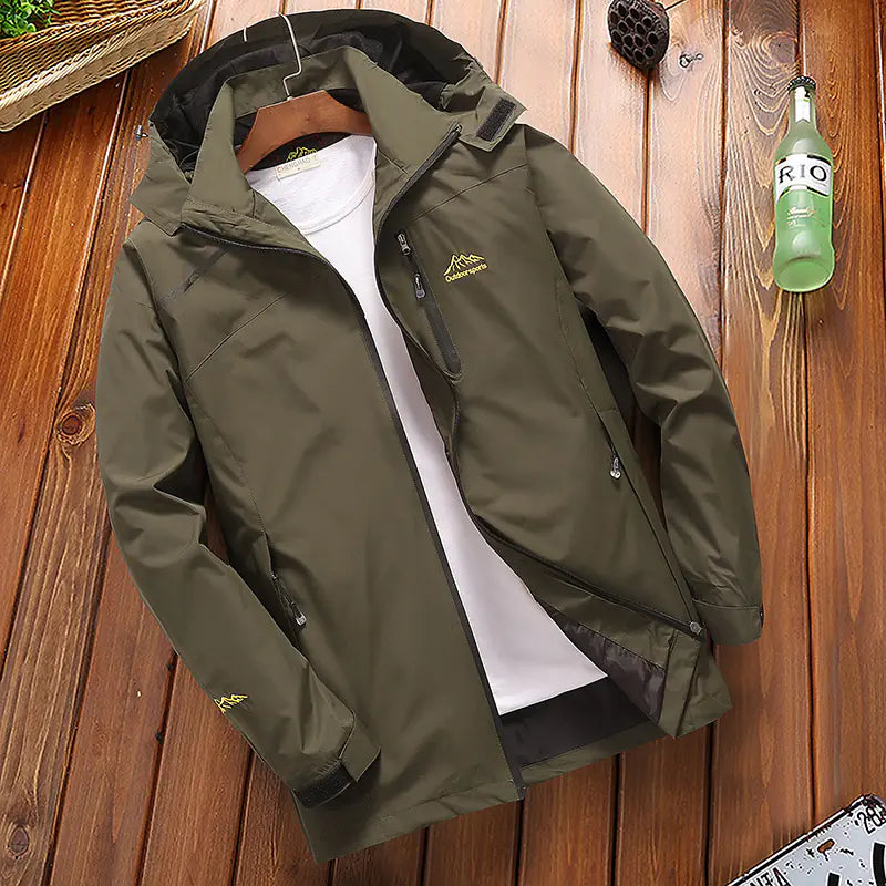 Men's loose outdoor windproof jacket displayed on a wooden surface, with a hood and zipper closure, in a green color.