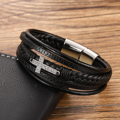 A men's retro braided leather and steel bracelet with a black color scheme, featuring a metallic clasp and a geometric pattern on the cross symbol, displayed on a wooden surface.