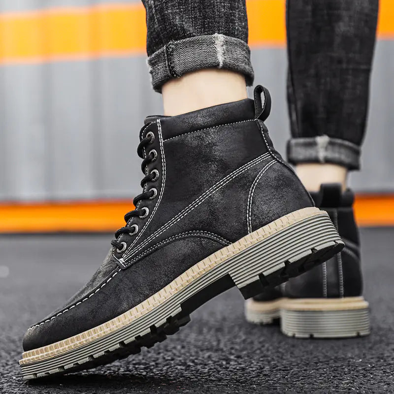 A pair of black men's casual leather boots with lace-up closure and flat heels, worn with rolled-up jeans.