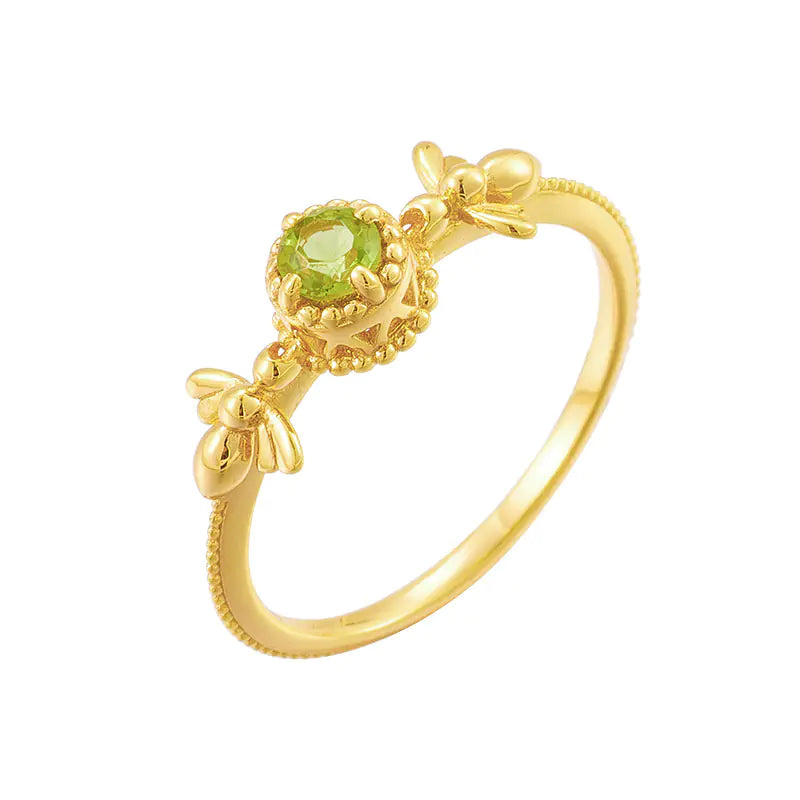 A gold-colored ring with a central green olivine stone, featuring intricate designs and a crown-like top.