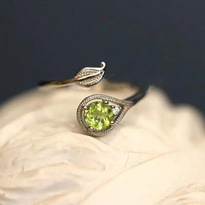 An olive green gemstone ring with a leaf and branch design on a wooden surface.