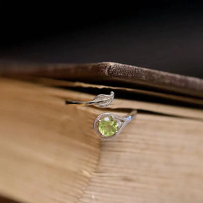 An olive green gemstone ring with a leaf and branch design on a wooden surface.