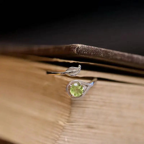 An olive green gemstone ring with a leaf and branch design on a wooden surface.
