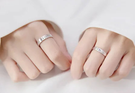 Two hands wearing adjustable couple rings with a cute kitten design on a white surface.