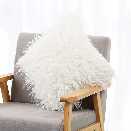 A white plush cushion cover with a long wool-like texture, displayed on a gray armchair.