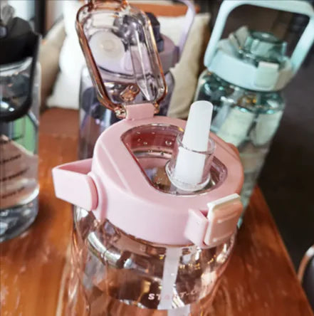 A large plastic water bottle with a pink and clear design, featuring a flip-top lid with a white spout and a pink carrying loop.