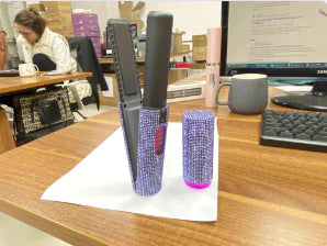 A portable USB hair straightener with a pink and black design, displayed on a table next to its charging base.