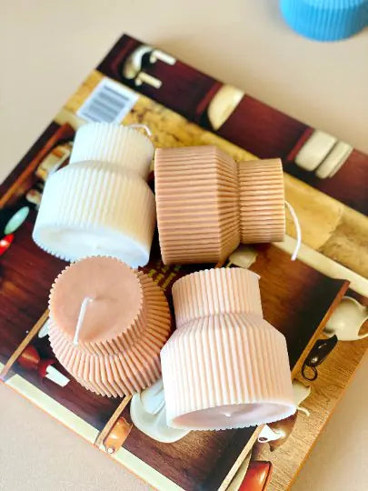 A group of ribbed pedestal pillar candles in various colors, displayed on a wooden surface.
