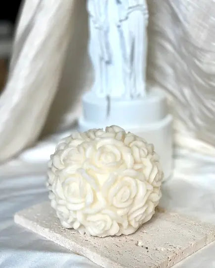 A pink scented candle shaped like a rose blossom, placed on a white surface with a blurred background.
