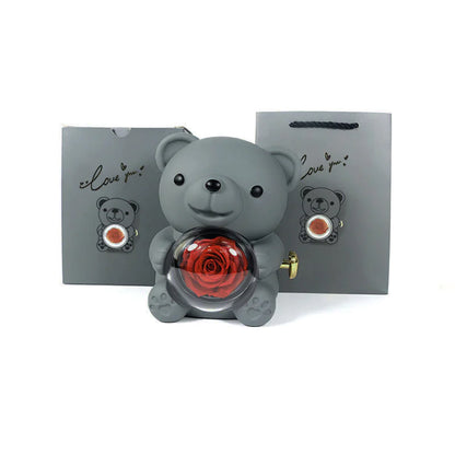 A gray bear-shaped plastic jewelry box with a red rose inside, displayed alongside its packaging that also features the image of the bear and rose.