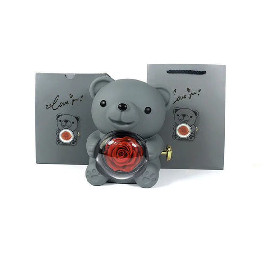 A gray bear-shaped plastic jewelry box with a red rose inside, displayed alongside its packaging that also features the image of the bear and rose.