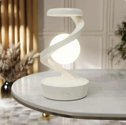 A modern, minimalist desk lamp with a unique rotating moon design, emitting a soft white light, placed on a marble surface.