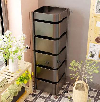 A black rotating snack storage rack with dimensions labeled on the image, placed on a wooden floor next to a bed with a yellow lamp on top.