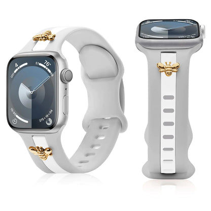 A silicone strap for Apple Watch Bands in gray and white, featuring gold honey bee charms on the clasp.
