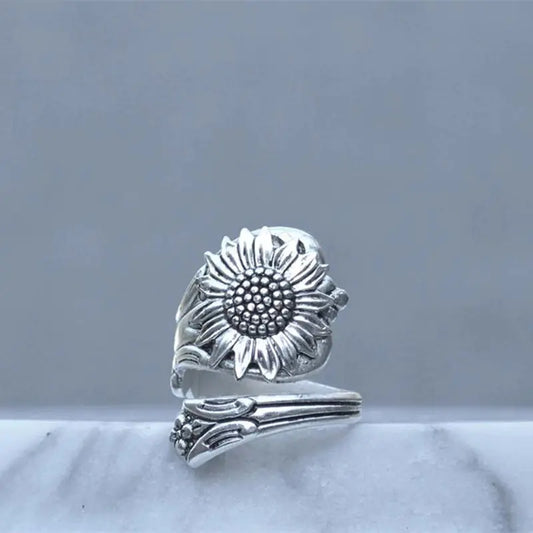 A silver ring with a daisy design, featuring an adjustable band and a prominent floral pattern on the top.