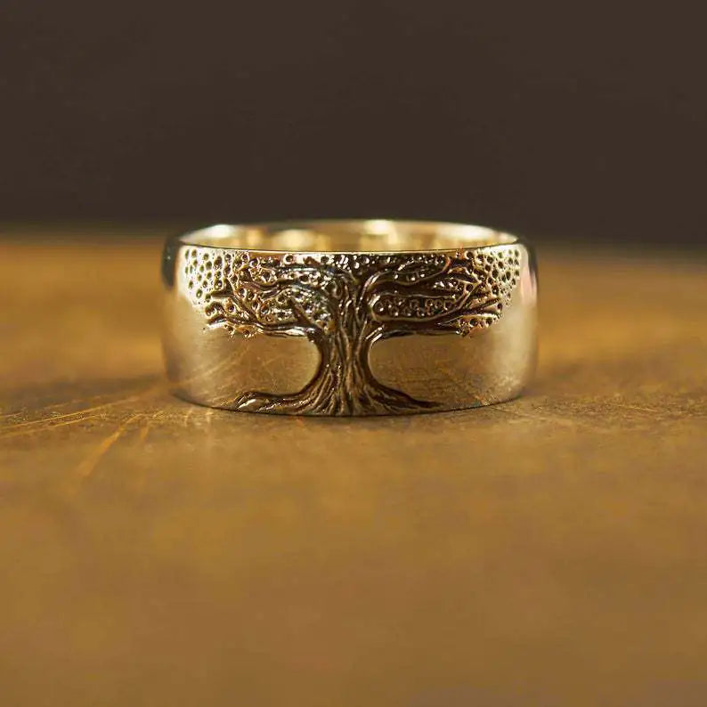 A gold-colored ring with a carved tree of life design on a wooden surface.