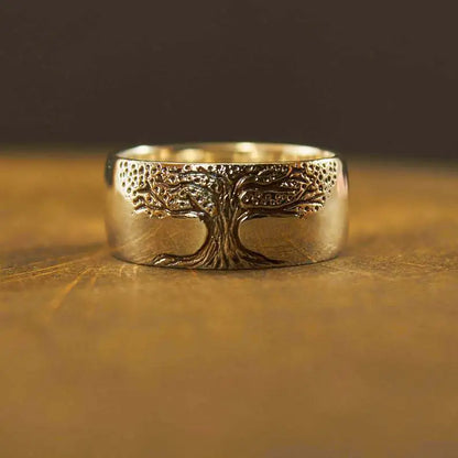 A gold-colored ring with a carved tree of life design on a wooden surface.