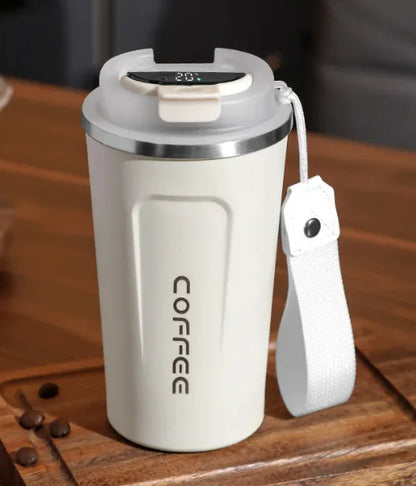 A white stainless steel vacuum coffee cup with a lid and a carrying strap, placed on a wooden surface with coffee beans scattered around it.