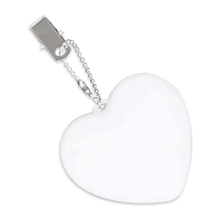 An LED automatic sensor purse light in a heart shape is illuminated and placed on an open book. The surrounding area includes a cup of coffee, glasses, and decorative flowers.