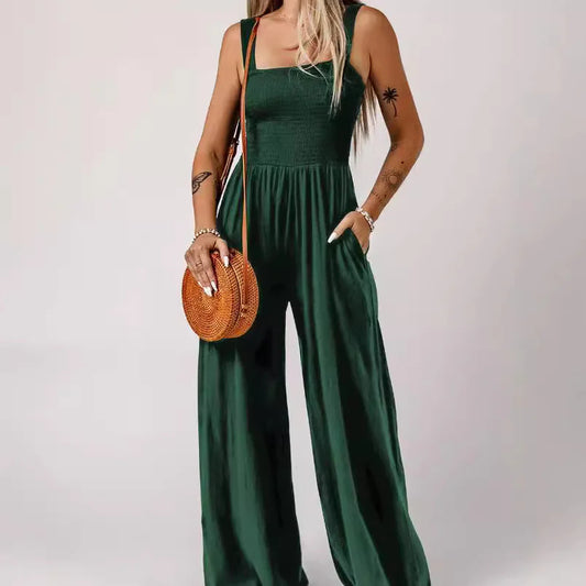 A woman wearing a green sleeveless square neckline smocked bodice wide-leg jumpsuit with pockets.